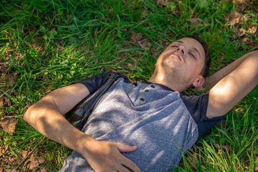 drunk man with a bottle of alcohol under his arm resting on a green field.