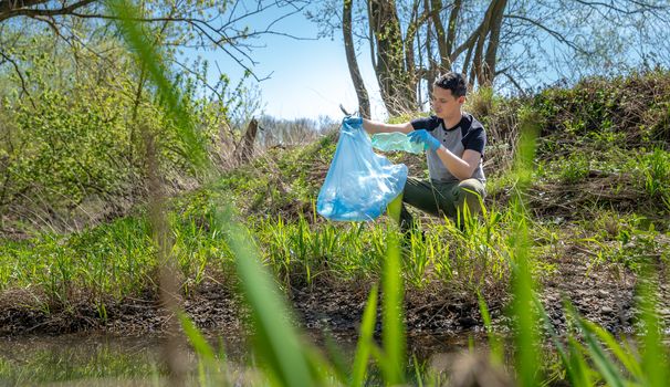 collecting garbage in a plastic bag, a volunteer man helps in the forest on the river bank.