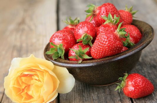 Bowl with fresh strawberries and yellow rose