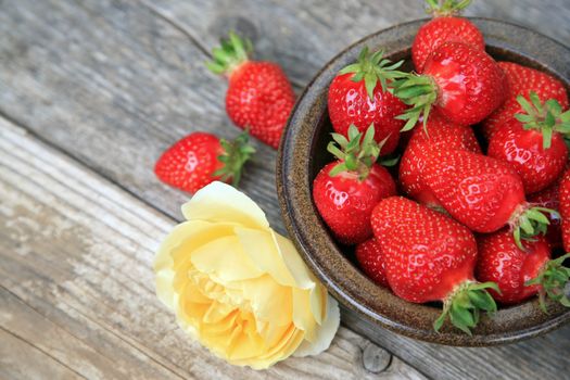Bowl with fresh strawberries and yellow rose