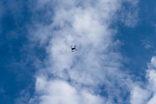quadrocopter flying against a blue sky with white clouds