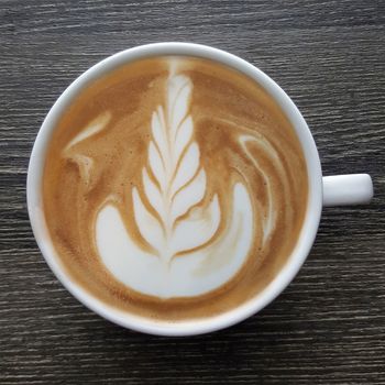 Top view of a mug of latte art coffee on timber background.