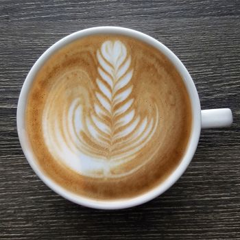 Top view of a mug of latte art coffee on timber background.