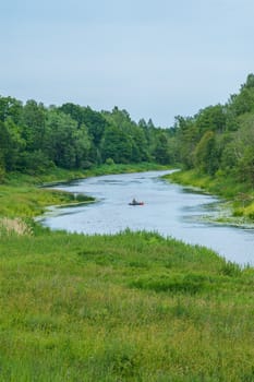 river among the green banks and the fisherman on a boat in the distance