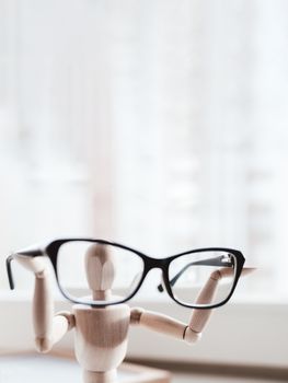 Wooden dummy with eyeglasses in hands. Mannequin presents glasses as a help for comfort life in case of poor vision. Miniature model of human as concept symbol of ophthalmology.