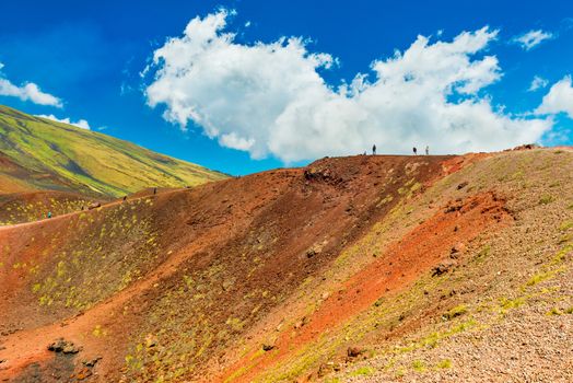 Beautiful colorful lava hills with group of people hiking to a volcanic crater. Mount Etna, Sicily, Italy