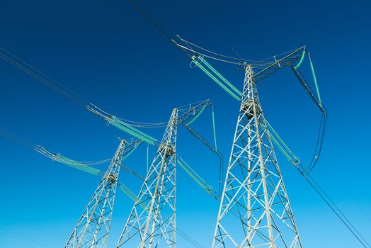 High voltage power lines with blue sky on the background, three electricity pylons