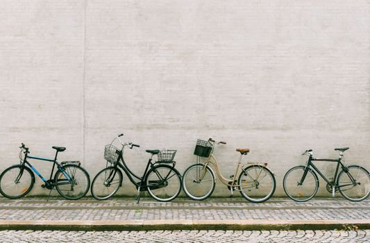 Four bicycles stand near a white brick wall. Several different bikes parked along an empty street in Copenhagen
