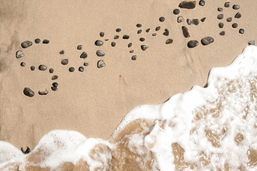 Summer word written on the sand with dark stones, in a beach. Summer idea and atmosphere.