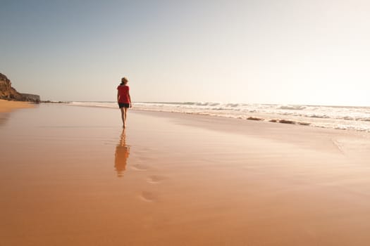 Solitary girl on beach looking at the sea with her reflection. Sunset time.