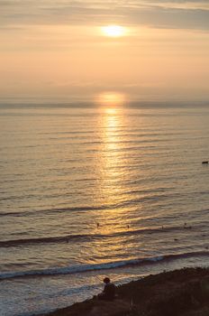 Man sitting at the foot of the sea watching the sunset