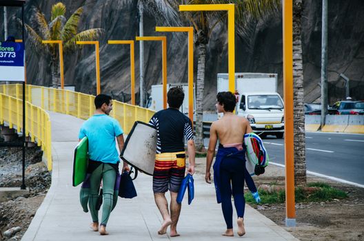 three surfers boys walking towards the sea