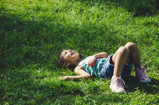 Laughing little girl lying on the grass in the park