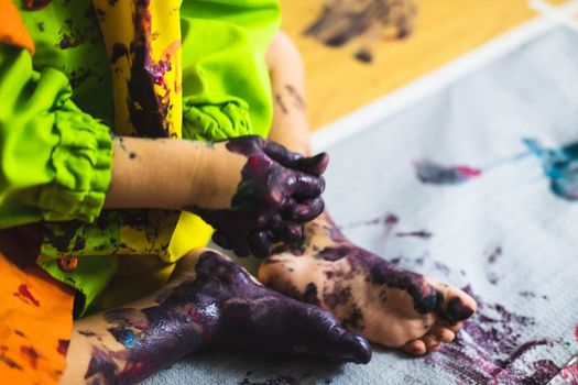 Chlid playing with different color paintings ends with multicolor hands and feet
