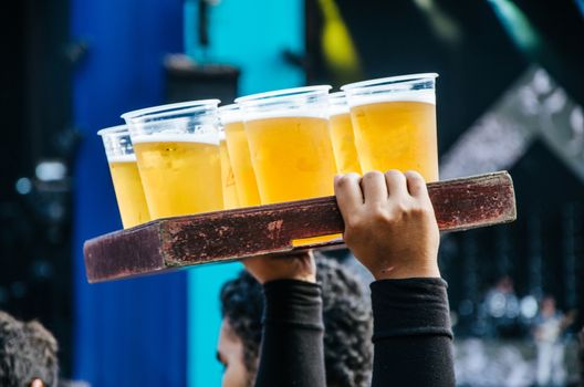 Beer seller with many plastic cups with beer in a wooden box at a concert