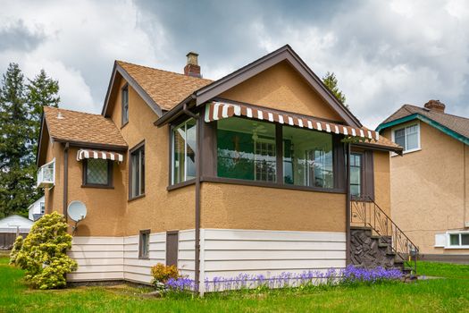 Modest family house with green lawn in front. Old residential house on cloudy day in Canada