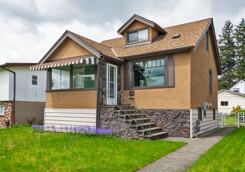 Modest family house with green lawn in front. Old residential house on cloudy day in Canada