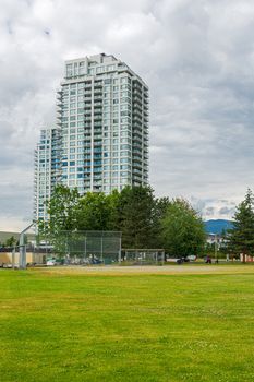 New residential high-rise buildings with green lawn of park in front. Condo building with cars parked on the street on cloudy sky background