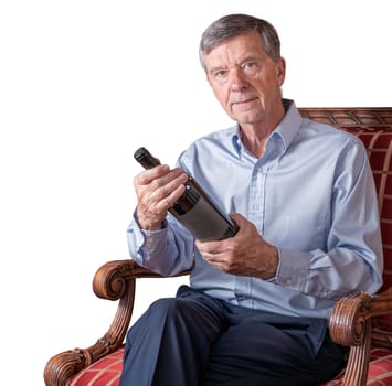 Friendly senior retired man examining a wine bottle label while seated in chair and isolated or cutout against a white background