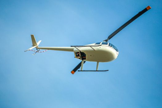 White helicopter flies in blue cloudless sky