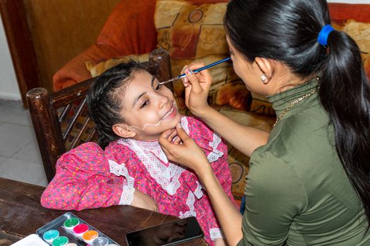 mother putting makeup of Catrina on her daughter's face to celebrate a festival