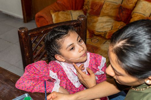 mother putting makeup of Catrina on her daughter's face to celebrate a festival