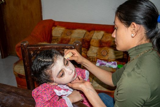 mother putting makeup of Catrina on her daughter's face to celebrate a festival