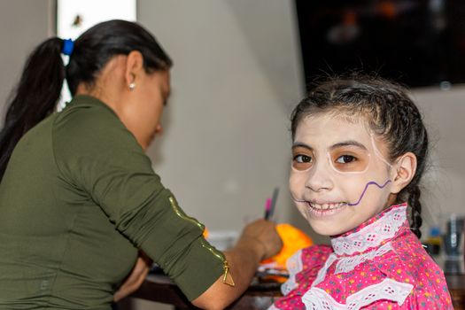 mother putting makeup of Catrina on her daughter's face to celebrate a festival