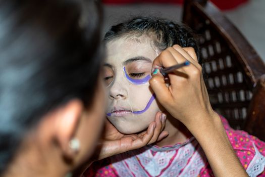 mother putting makeup of Catrina on her daughter's face to celebrate a festival