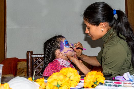 mother putting makeup of Catrina on her daughter's face to celebrate a festival