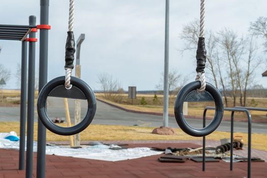 metal gymnastic rings hang on the outdoor sports field, which is being repaired and restored