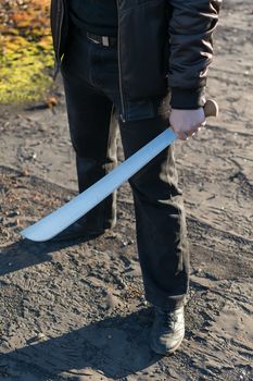 machete in the hand of a man on the street in black clothes and leather jacket