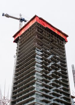 New residential building under construction with the crane above. High rise monolith concrete building on cast sky background