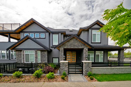 Entrance of luxury residential house with metal gate and stone texture walls. Big family house entrance with landscaped front yard