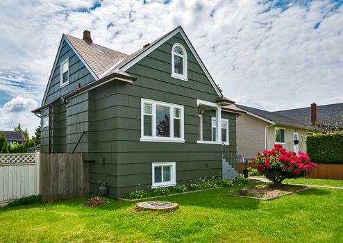 Old but neat residential house with concrete pathway over front yard lawn on cloudy day