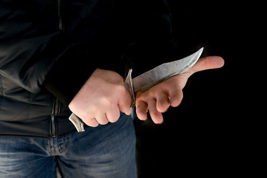 Crime, a man in a leather jacket and jeans in a dark room defiantly cuts his hand with a knife