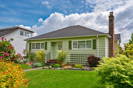 Perfect neighbourhood. Neat and nice average family house with green lawn in front. Old residential house on cloudy sky background