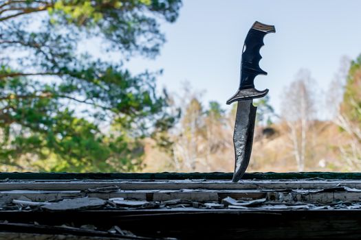 a terrible old combat knife stuck in the ruined window sill of an abandoned house on the background of tree branches outside the window