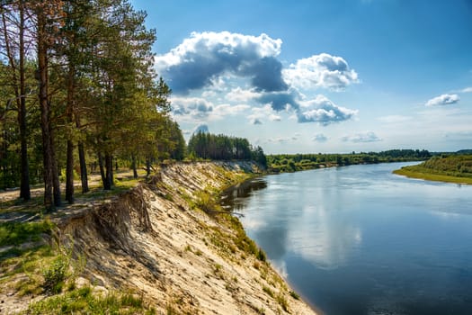 High steep river bank covered with forest and a view of the river and the horizon on a sunny summer day