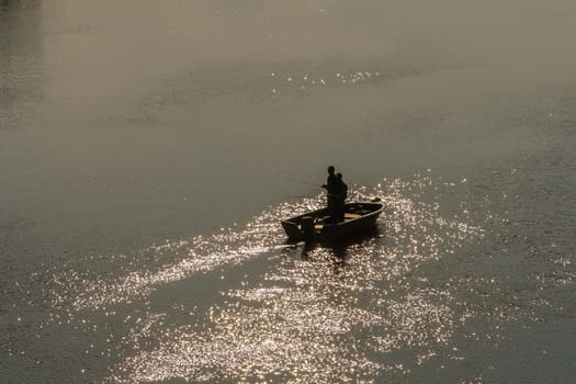 fishermen with fishing rods on a boat in the middle of the river, sunset backlit shooting
