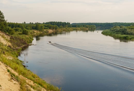 riverbank and a motor boat goes on the water, leaving a mark