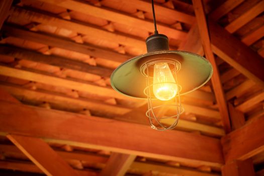 Incandescent light bulb hanging from ceiling over head from roof house gable corner at Asian countryside. Incandescent light bulb, old style and low technology. Edison lamp.