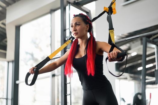 Athlete woman training exercising with suspension system indoor gym. Beautiful caucasian sportive woman do stretching strenght exercise with special strap. Middle age girl workout