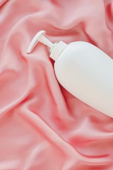 Blank label cosmetic container bottle as product mockup on pink silk background, hygiene and healthcare