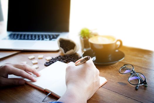 Male manager putting his ideas and writing business plan at workplace,man holding pen and making note in notebook , on the table in office,vintage color,morning light ,selective focus.