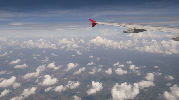 Plane travel concept : View from aircraft window. Clouds and blue sky under airplane wing as seen through window of an airplane in wide angel with copy space for travel agency background