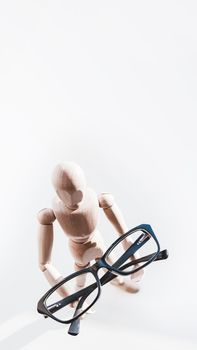 Wooden dummy with eyeglasses in hands. Mannequin presents glasses as a help for comfort life in case of poor vision. Miniature model of human as concept symbol of ophthalmology.