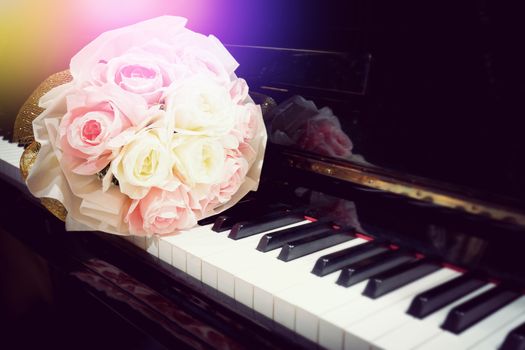 Rose flower in bouquet on keyboard of piano with light flare in concert performance. Selective focus image. Warm color tone music background