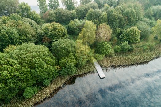 Photo taken from the air with the drone, fishing jetty at a pond with cloud reflections and a forest with green trees on the shore.