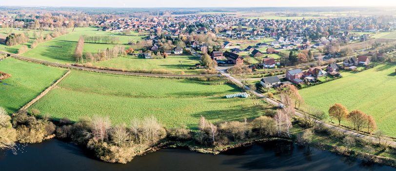 Aerial photo of a small village in Lower Saxony, Germany, with the shore of a pond and meadows in the foreground, taken with the drone